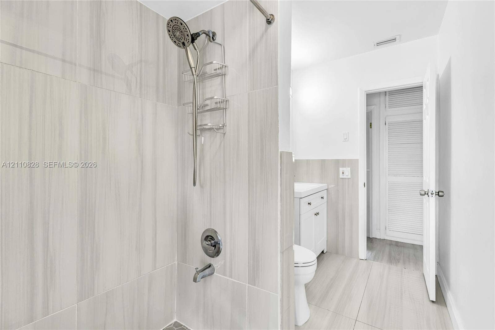 1600 NW 120th Avenue, Pembroke Pines, FL 33026 Bathroom featuring neutral large-format tile surround, chrome shower hardware, white vanity cabinetry, and louvered closet doors
