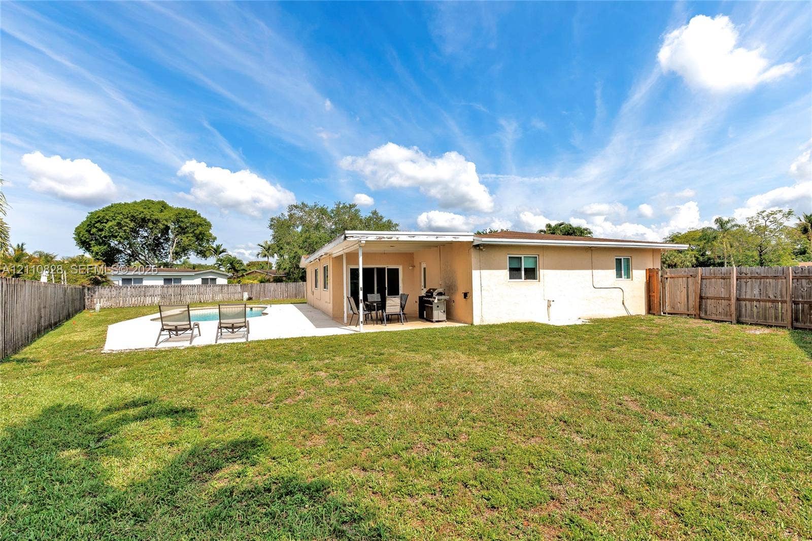 1600 NW 120th Avenue, Pembroke Pines, FL 33026 Rear exterior featuring a covered patio, concrete pool deck, in-ground pool, and wood privacy fencing surrounding the grass lawn