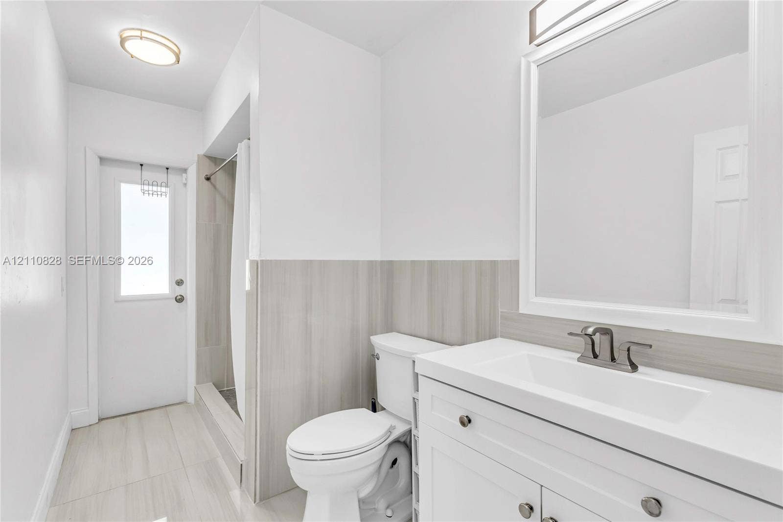 1600 NW 120th Avenue, Pembroke Pines, FL 33026 White vanity featuring an integrated sink, brushed metal faucet, and neutral-toned stone-finish backsplash, complemented by matching tile flooring, a tub-shower enclosure with tile surround, and a framed mirror