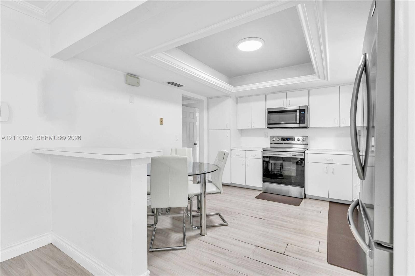1600 NW 120th Avenue, Pembroke Pines, FL 33026 Kitchen featuring white cabinetry, stainless steel appliances, tray ceiling, and wood-finish flooring with a peninsula counter