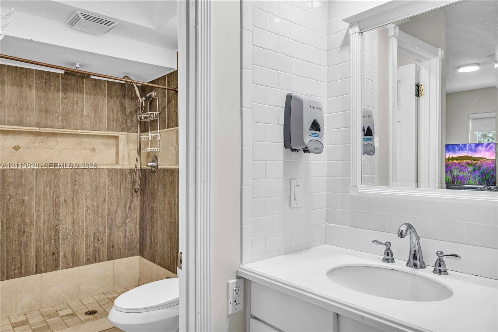 1600 NW 120th Avenue, Pembroke Pines, FL 33026 Bathroom featuring white subway tile walls, a vanity with an integrated basin, a framed mirror, and a walk-in shower with wood-finish wall paneling and a recessed niche
