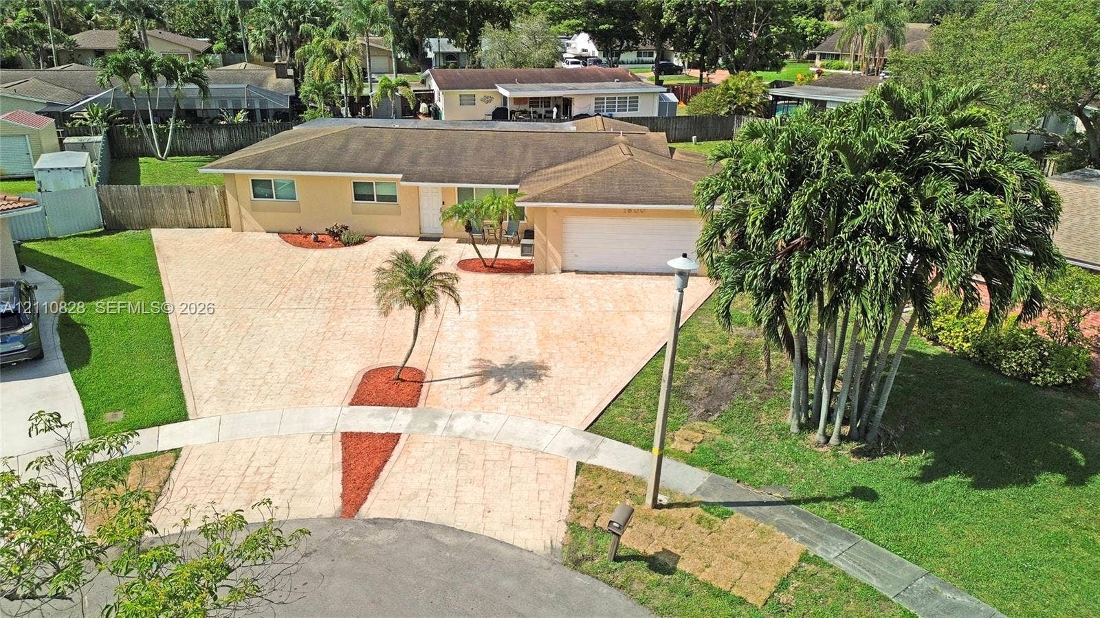 1600 NW 120th Avenue, Pembroke Pines, FL 33026 Single-story residence featuring a paver driveway, attached garage, manicured lawn, and mature palm landscaping