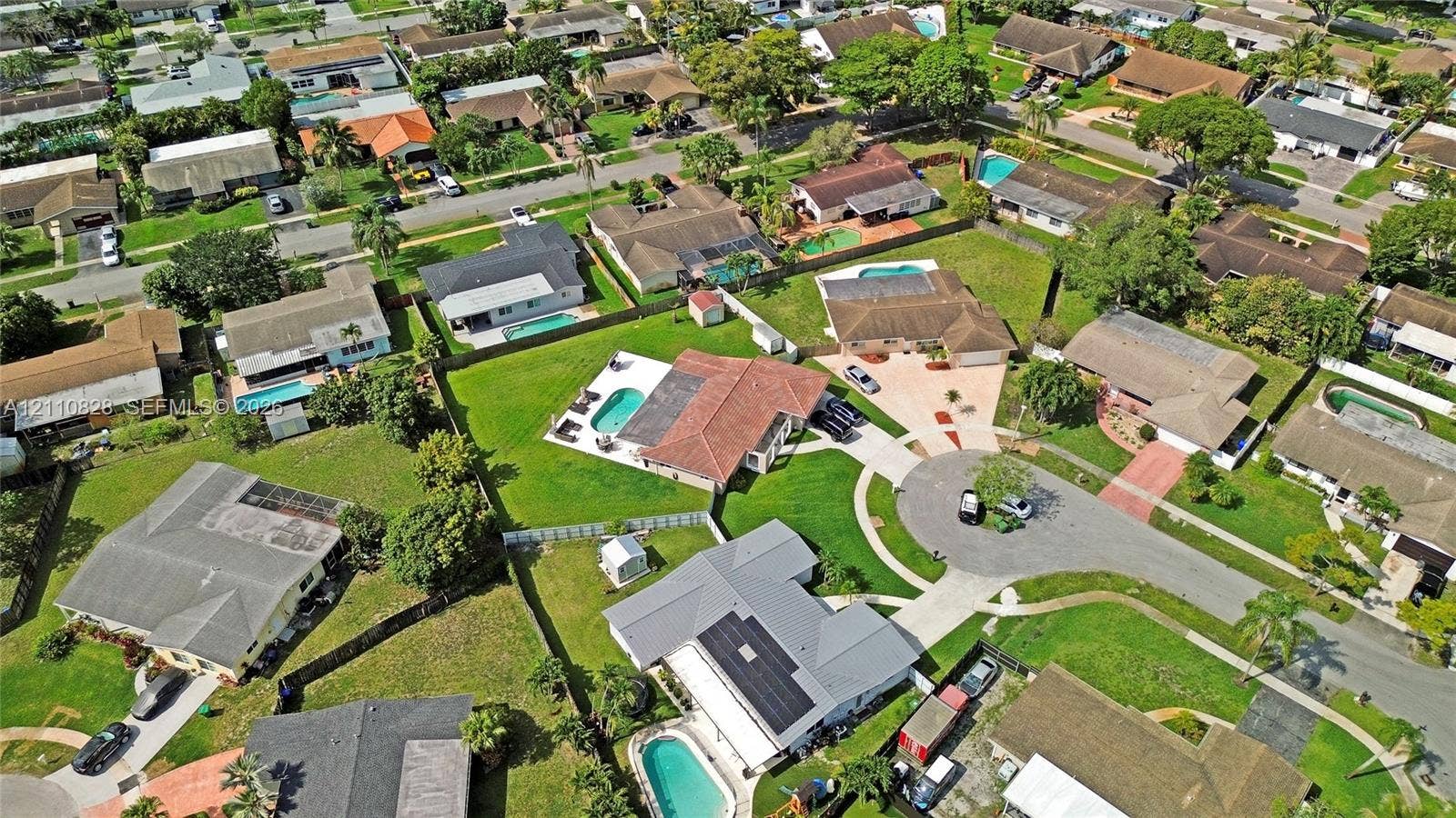 1600 NW 120th Avenue, Pembroke Pines, FL 33026 Aerial perspective of a residence featuring a clay tile roof, a rectangular swimming pool, a paved driveway, and a fenced-in grassy lawn