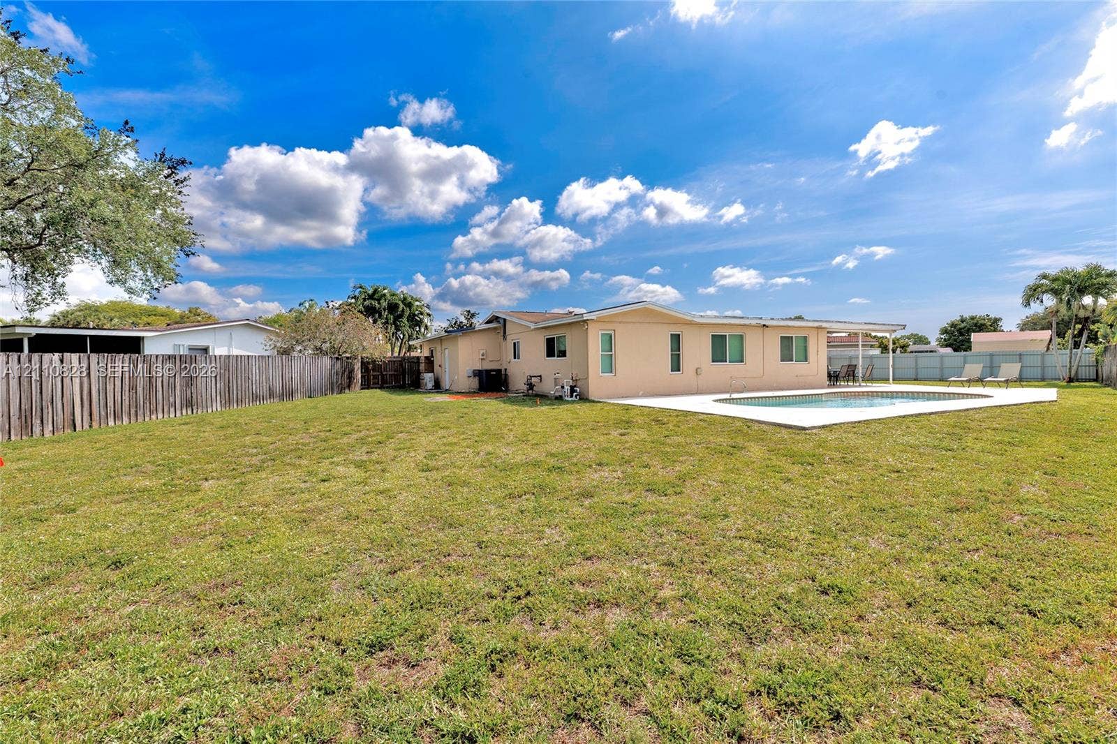 1600 NW 120th Avenue, Pembroke Pines, FL 33026 Expansive backyard featuring a concrete pool deck, in-ground swimming pool, wood privacy fencing, and a covered rear patio