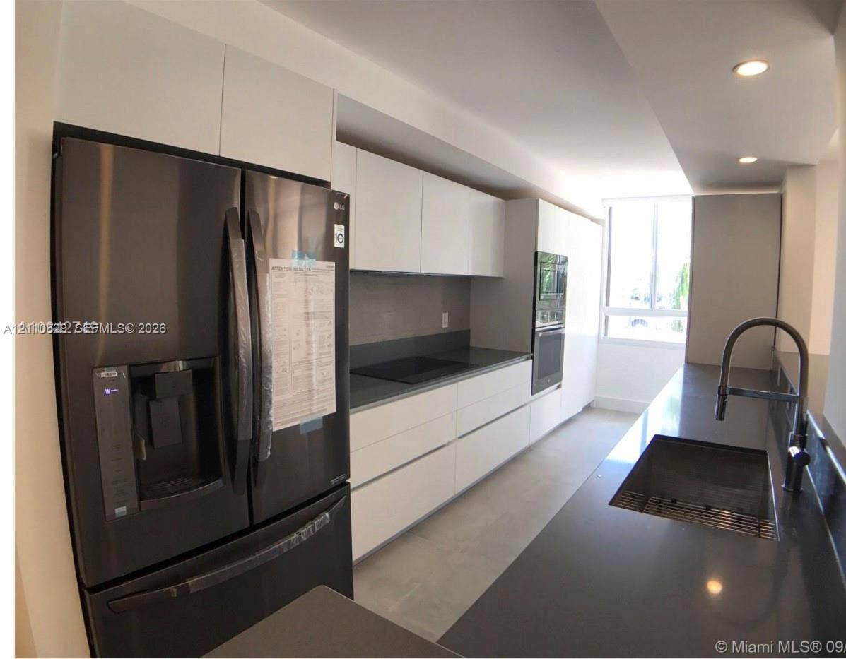 Modern kitchen featuring high-gloss white flat-panel cabinetry, dark solid-surface countertops, built-in stainless steel oven, integrated cooktop, and a matte black gooseneck faucet