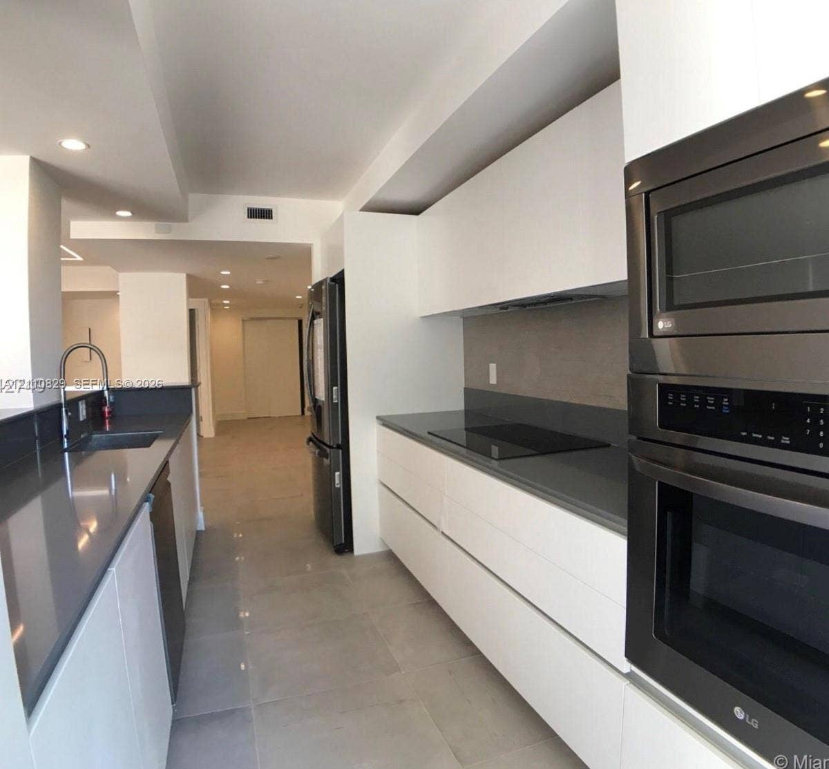 Sleek kitchen featuring flat-panel white cabinetry, quartz countertops, a smooth-surface cooktop, stainless steel wall-mounted oven and microwave, and large-format floor tile