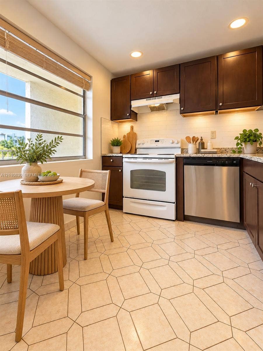 Kitchen featuring dark wood cabinetry, light-toned stone-finish countertops, geometric-patterned tile flooring, recessed ceiling lighting, and stainless steel dishwasher