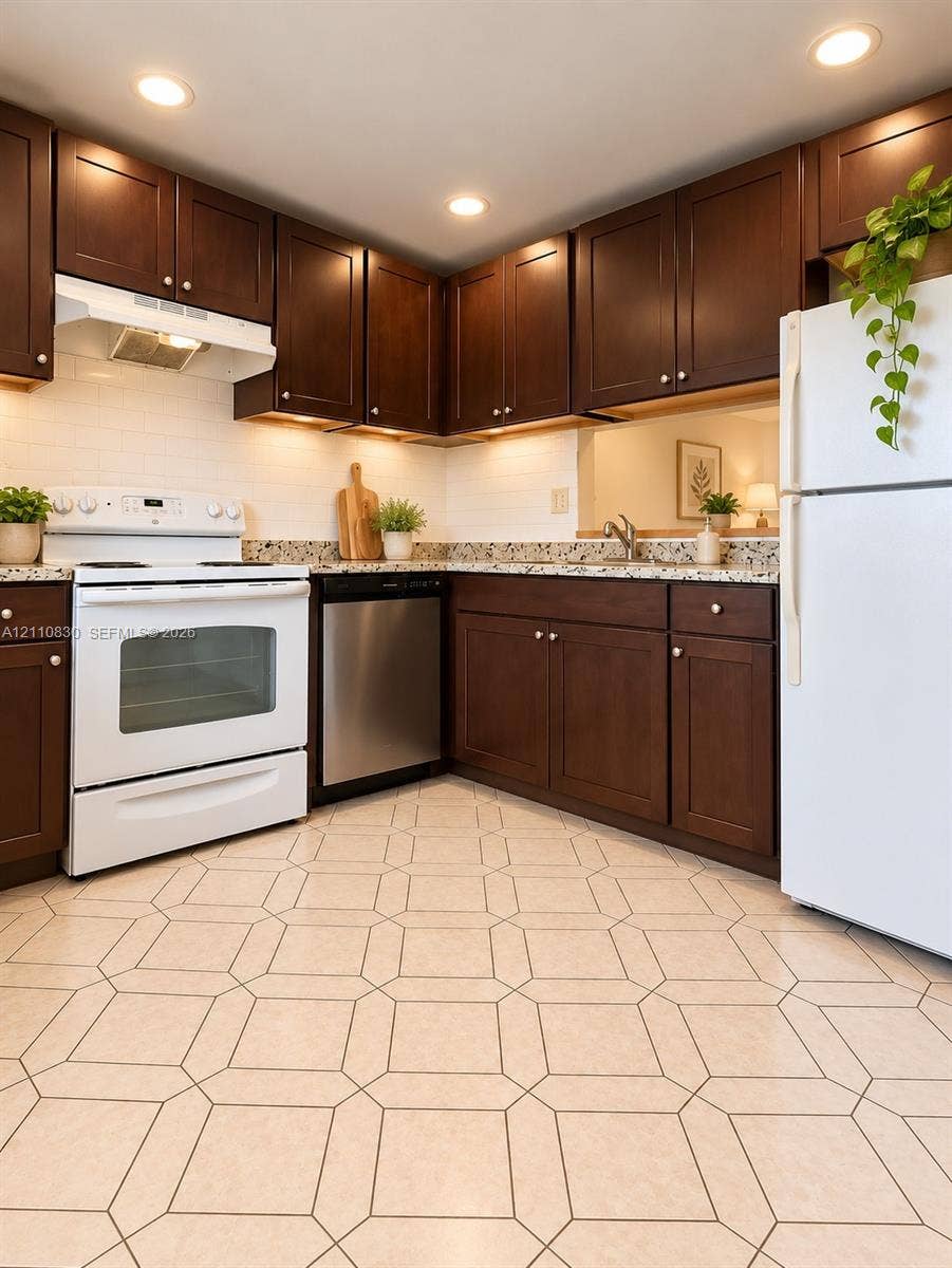 STAGED Kitchen featuring dark wood cabinetry, light stone-finish countertops, white subway tile backsplash, stainless steel dishwasher, and patterned tile flooring