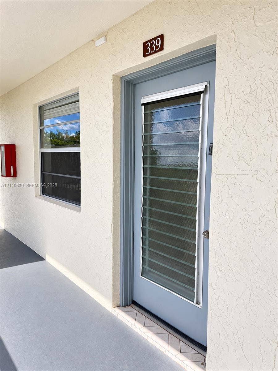 STAGED Textured stucco exterior wall with a blue entry door featuring integrated glass jalousie slats and a metallic door knob