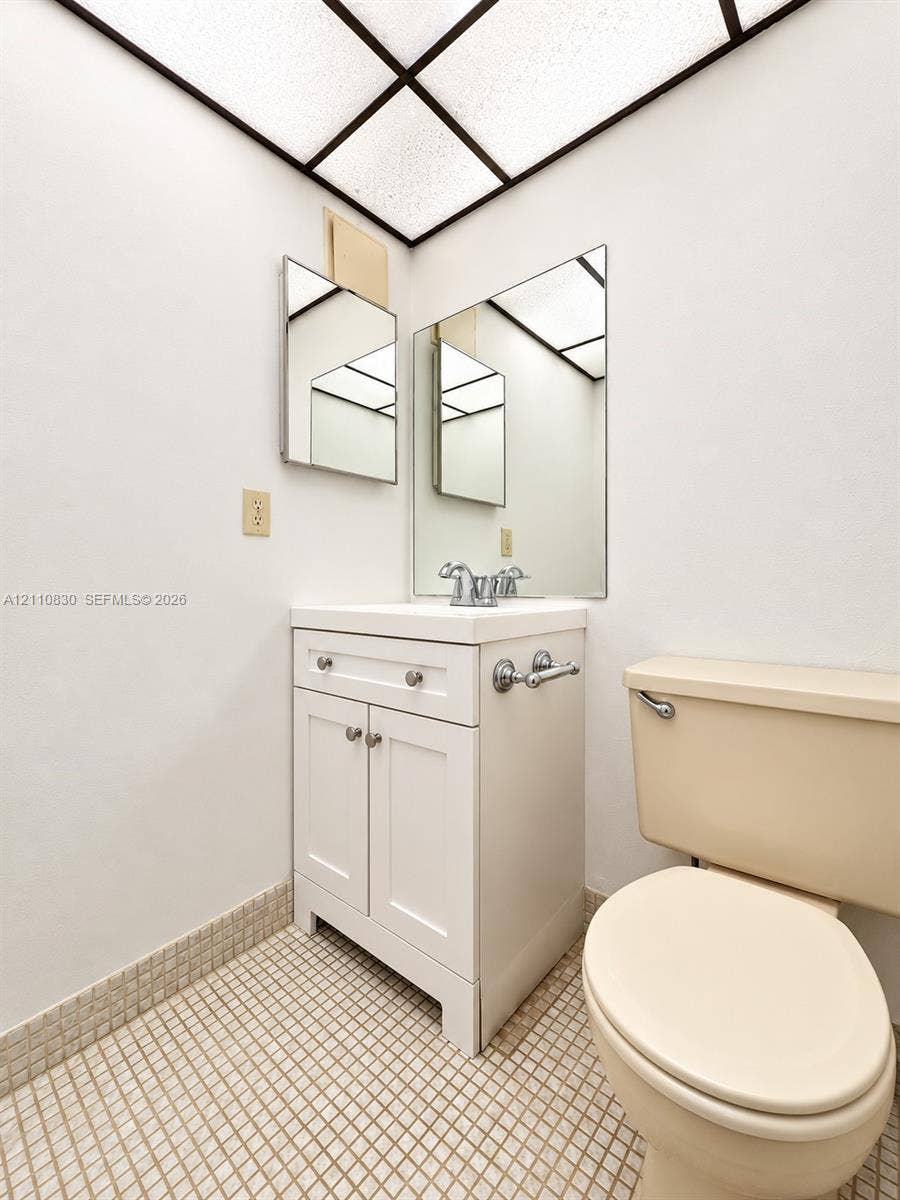 White shaker-style vanity with a square sink, chrome-finish dual-handle faucet, grid-pattern ceiling light, and mosaic-tiled flooring