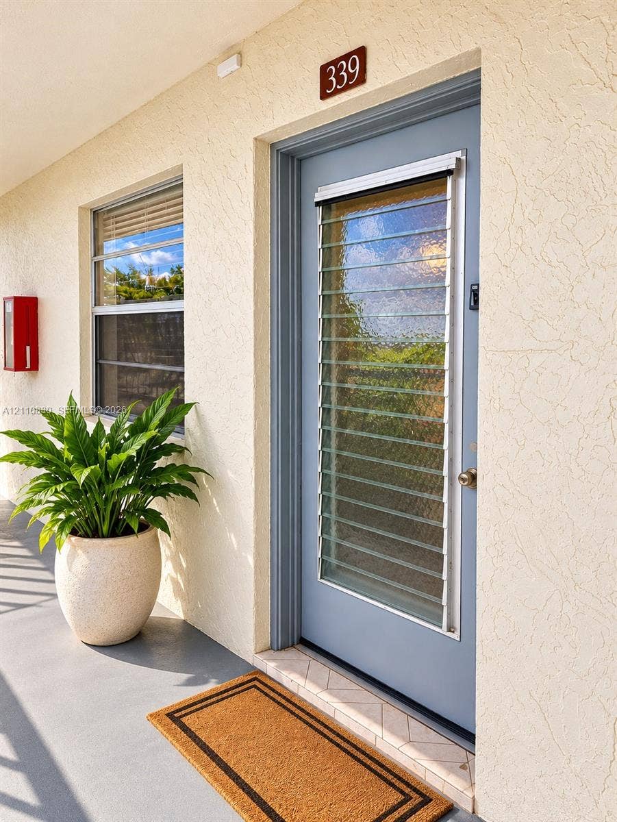 STAGED Textured stucco exterior wall with a blue entry door featuring integrated glass jalousie slats and a metallic door knob