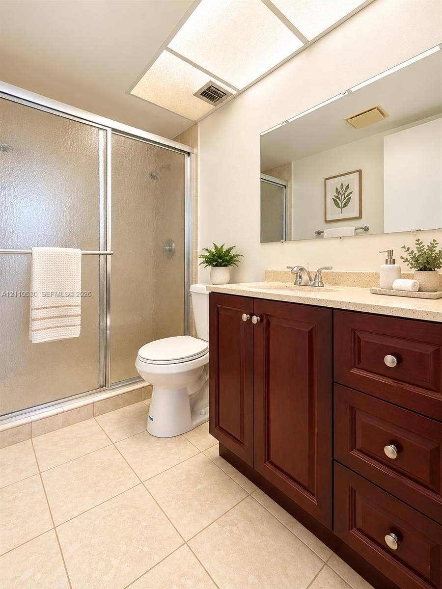 STAGED Bathroom featuring a dark wood-finish vanity with stone-composite countertop, full-width mirror, tile flooring, and a glass-enclosed shower