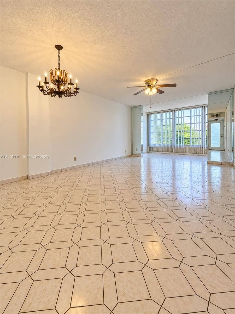 Spacious interior featuring patterned tile flooring, a multi-arm candelabra-style chandelier, a ceiling fan with integrated lighting, and floor-to-ceiling windows with vertical blinds