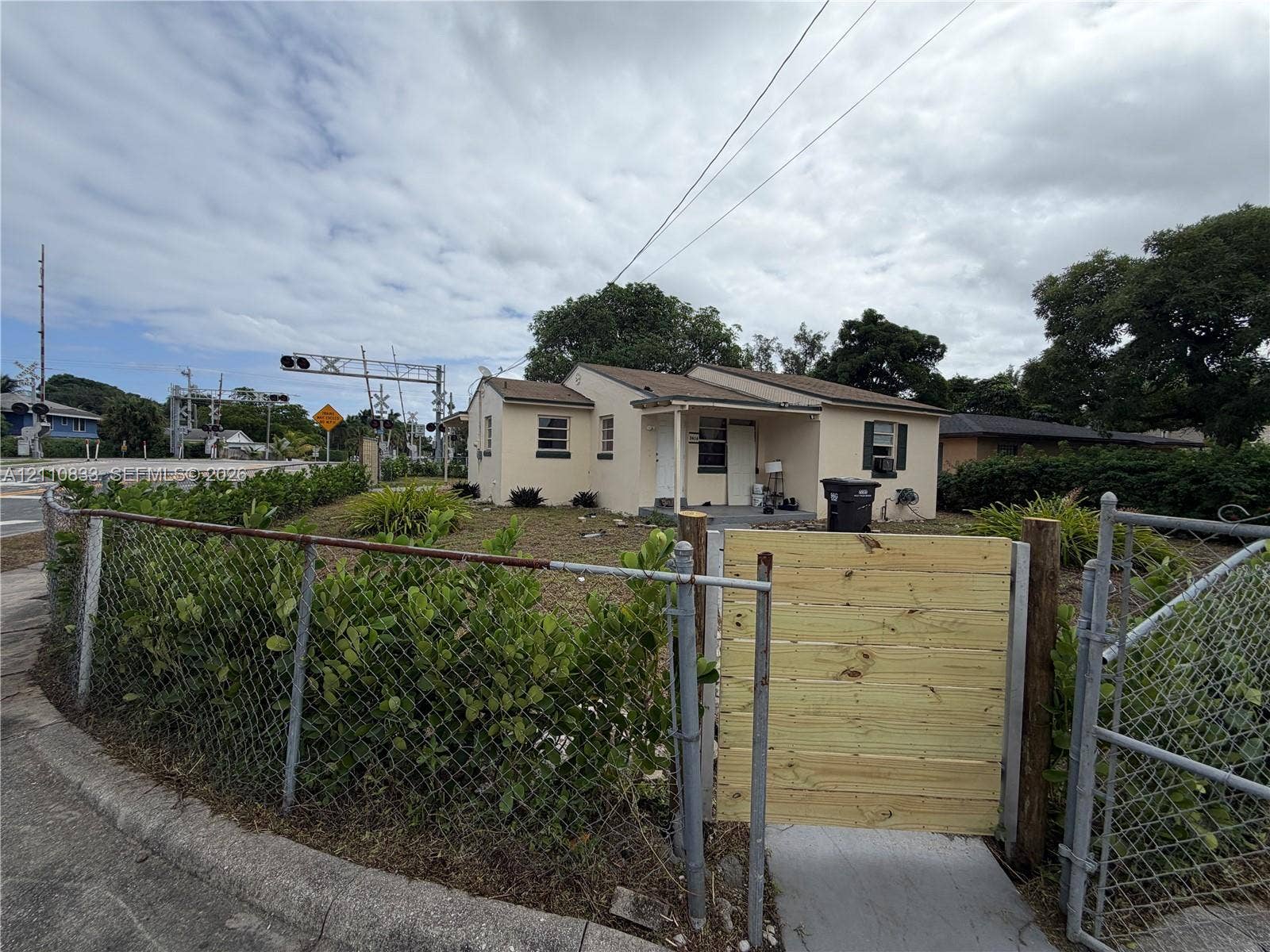 Exterior featuring a stucco facade, covered front entryway, and metal-framed chain-link fencing with a horizontal wood-slat gate