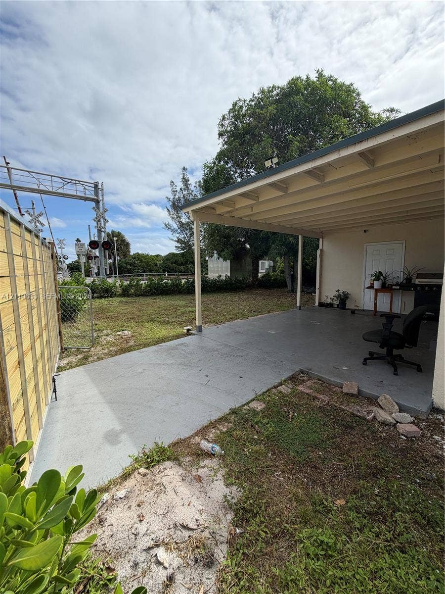 Covered concrete patio featuring an open-air design, wood-frame structural posts, and exterior privacy fencing