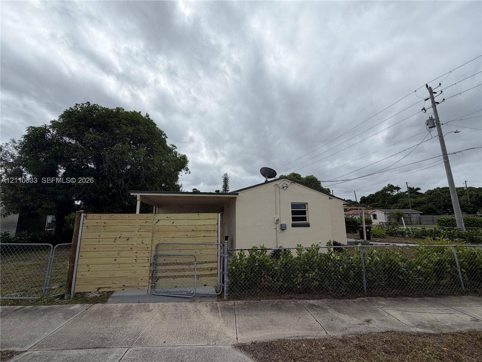 Stucco exterior with a covered side porch, horizontal wood-slat privacy fencing, and chain-link perimeter fencing