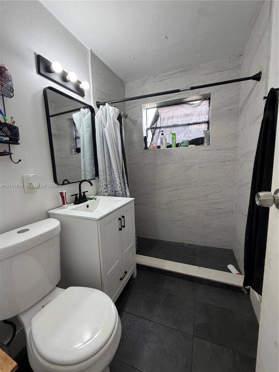 Bathroom featuring white cabinetry, a rectangular sink with matte black hardware, a black-framed vanity mirror, dark floor tile, and wall-tiled shower surround