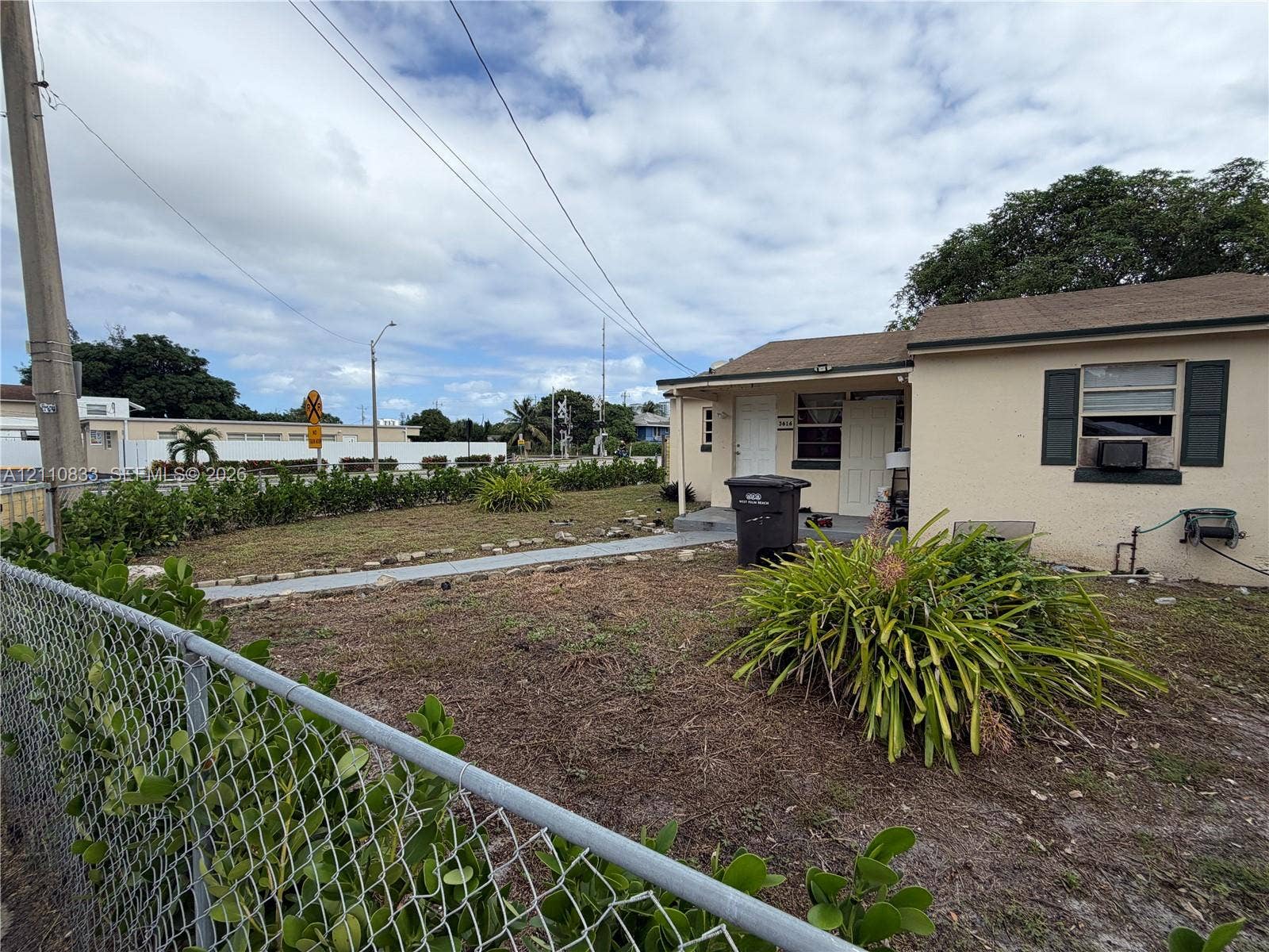 Single-story exterior featuring a light-toned stucco facade, dark-toned shutters, and a chain-link perimeter fence