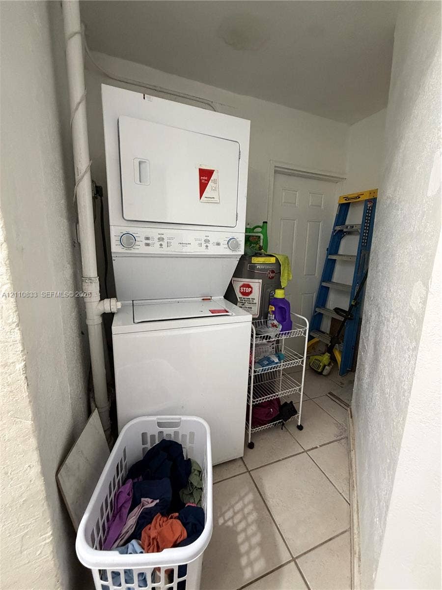 Stacked laundry unit on tile flooring featuring a six-panel door