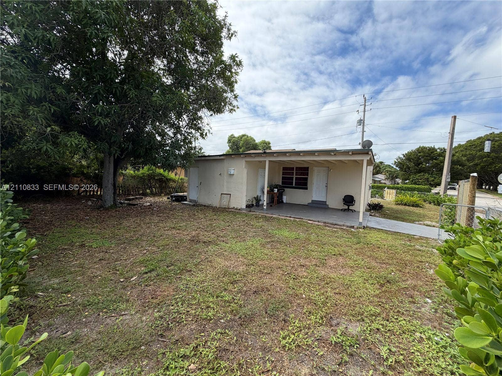 Exterior property featuring a covered patio, concrete walkway, and mature trees situated on a parcel with perimeter fencing