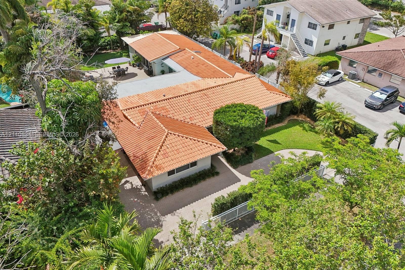 4120 SW 15th Street, Miami, FL 33142 Aerial perspective of a single-story residence featuring a terracotta tile roof, paved driveway, expansive manicured lawn, and mature landscaping