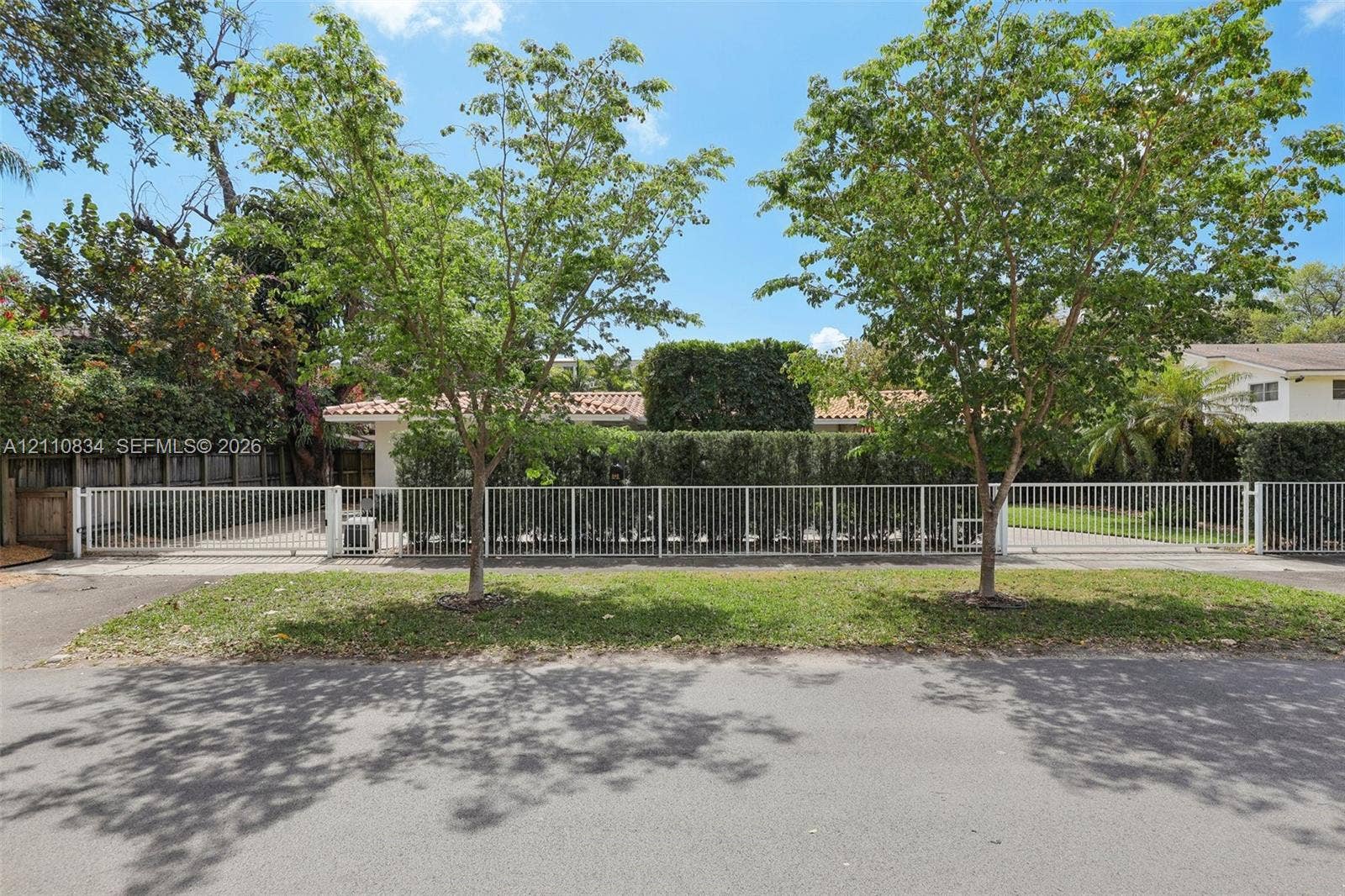 4120 SW 15th Street, Miami, FL 33142 White metal perimeter fencing, gated driveway access, mature landscaping, and established trees