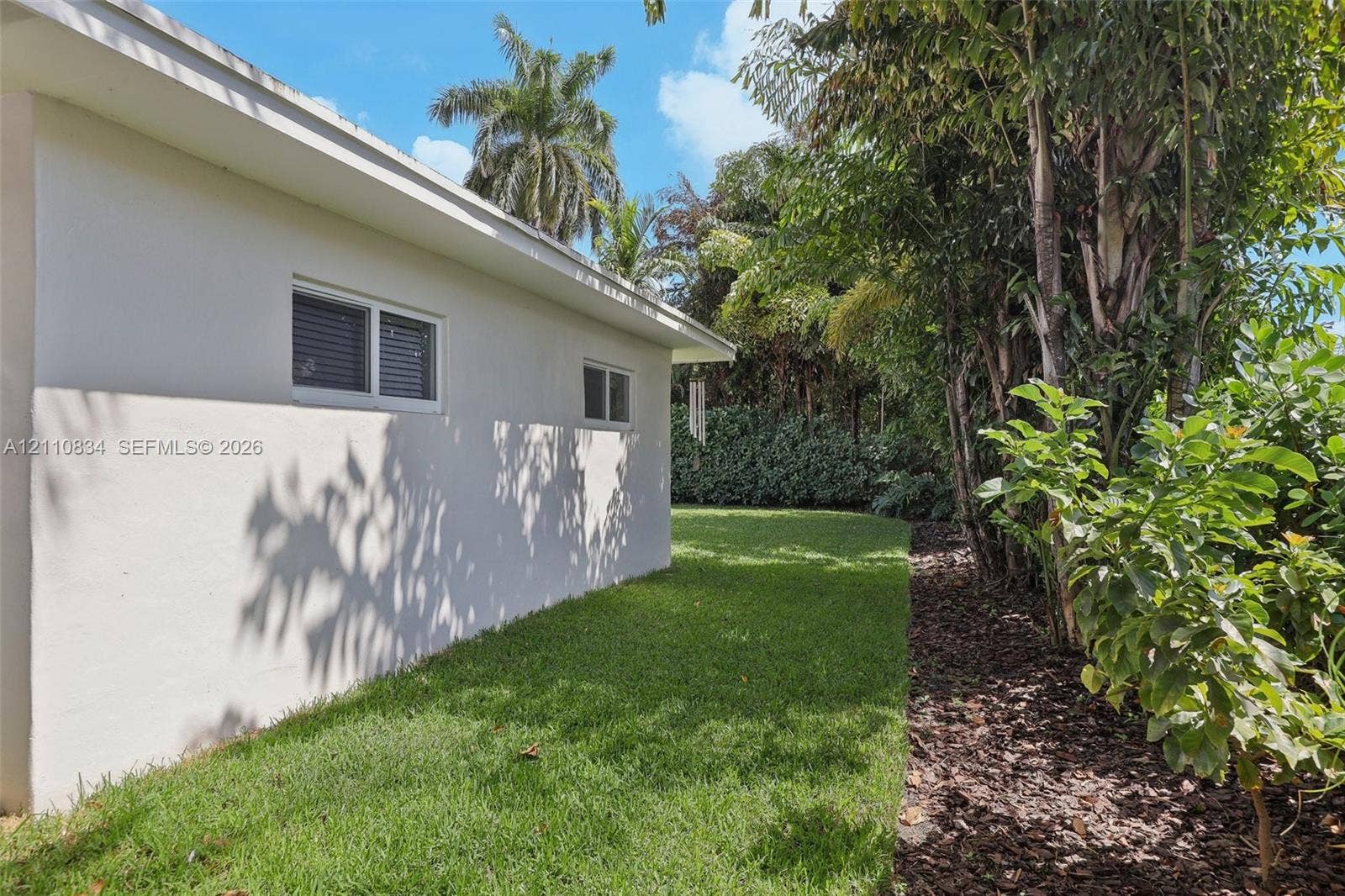 4120 SW 15th Street, Miami, FL 33142 Side exterior featuring stucco siding, white-trimmed horizontal sliding windows, a manicured lawn, and mature perimeter landscaping