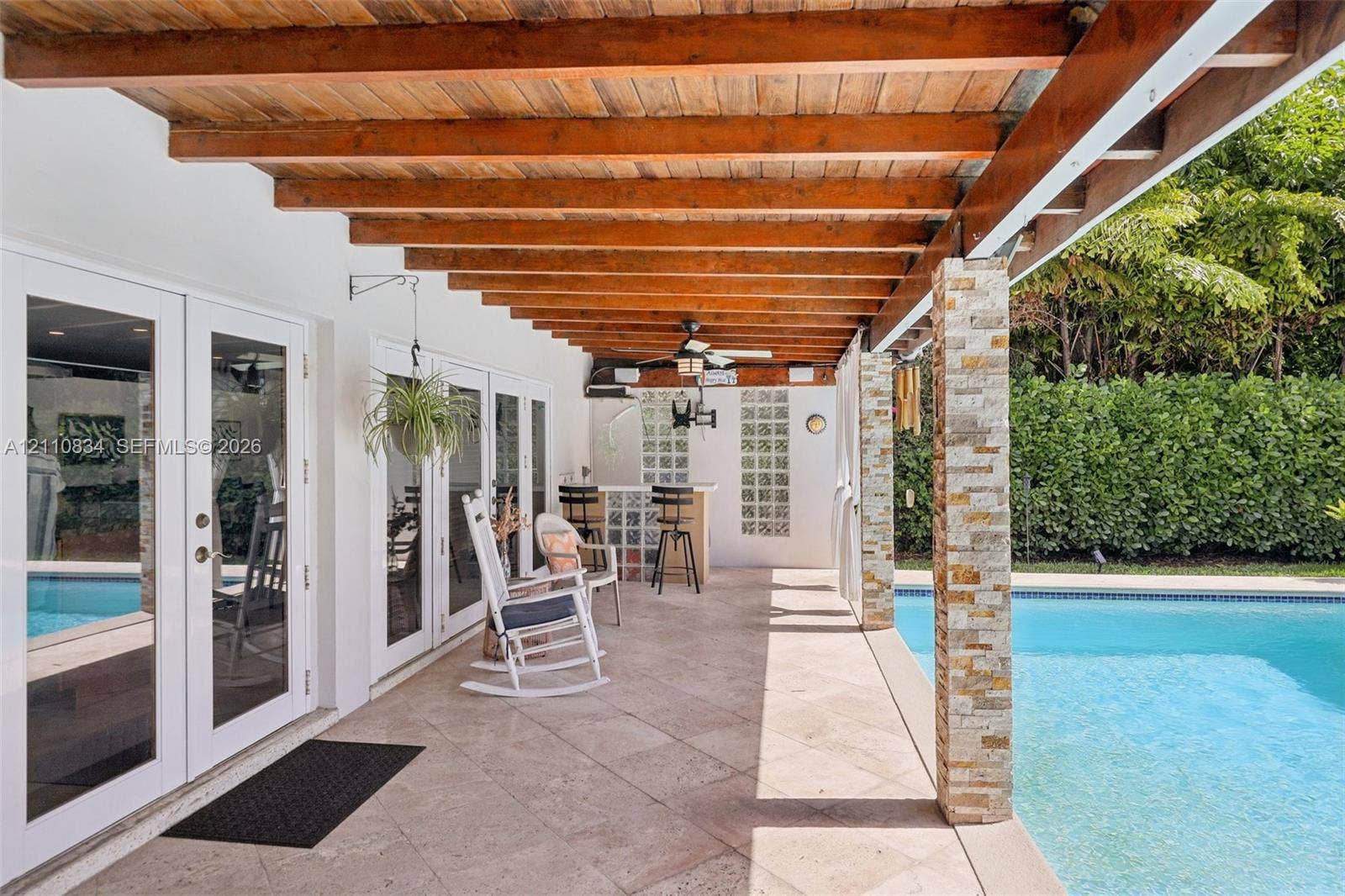 4120 SW 15th Street, Miami, FL 33142 Covered patio featuring a wood-beam pergola, stone-clad support columns, natural stone flooring, and built-in glass block bar, complemented by a swimming pool