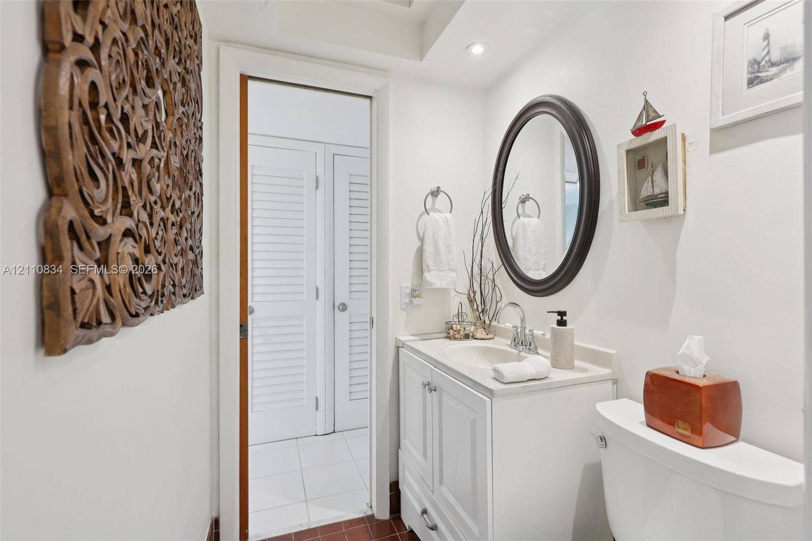 4120 SW 15th Street, Miami, FL 33142 Bathroom featuring a vanity with an integrated basin, a polished chrome faucet, an oval wall-mounted mirror, and louvered closet doors