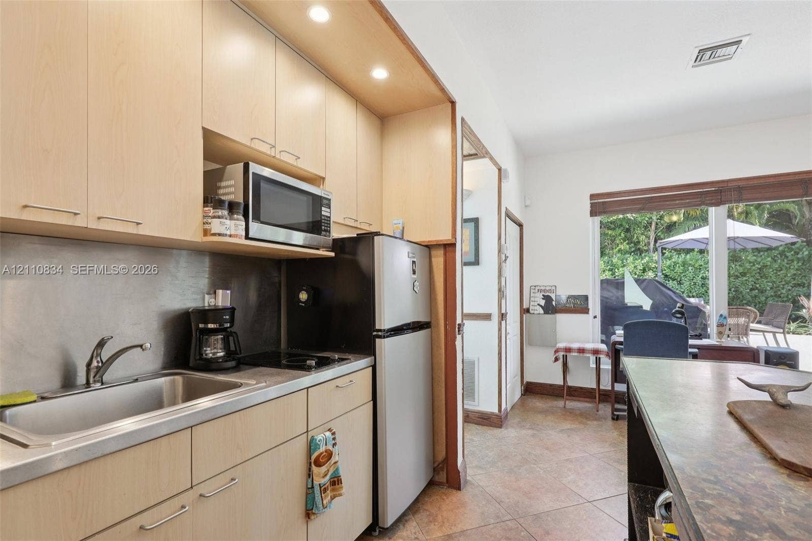4120 SW 15th Street, Miami, FL 33142 Kitchenette featuring light wood-finish cabinetry, stainless steel sink with arched faucet, metallic backsplash, built-in microwave, and tile flooring