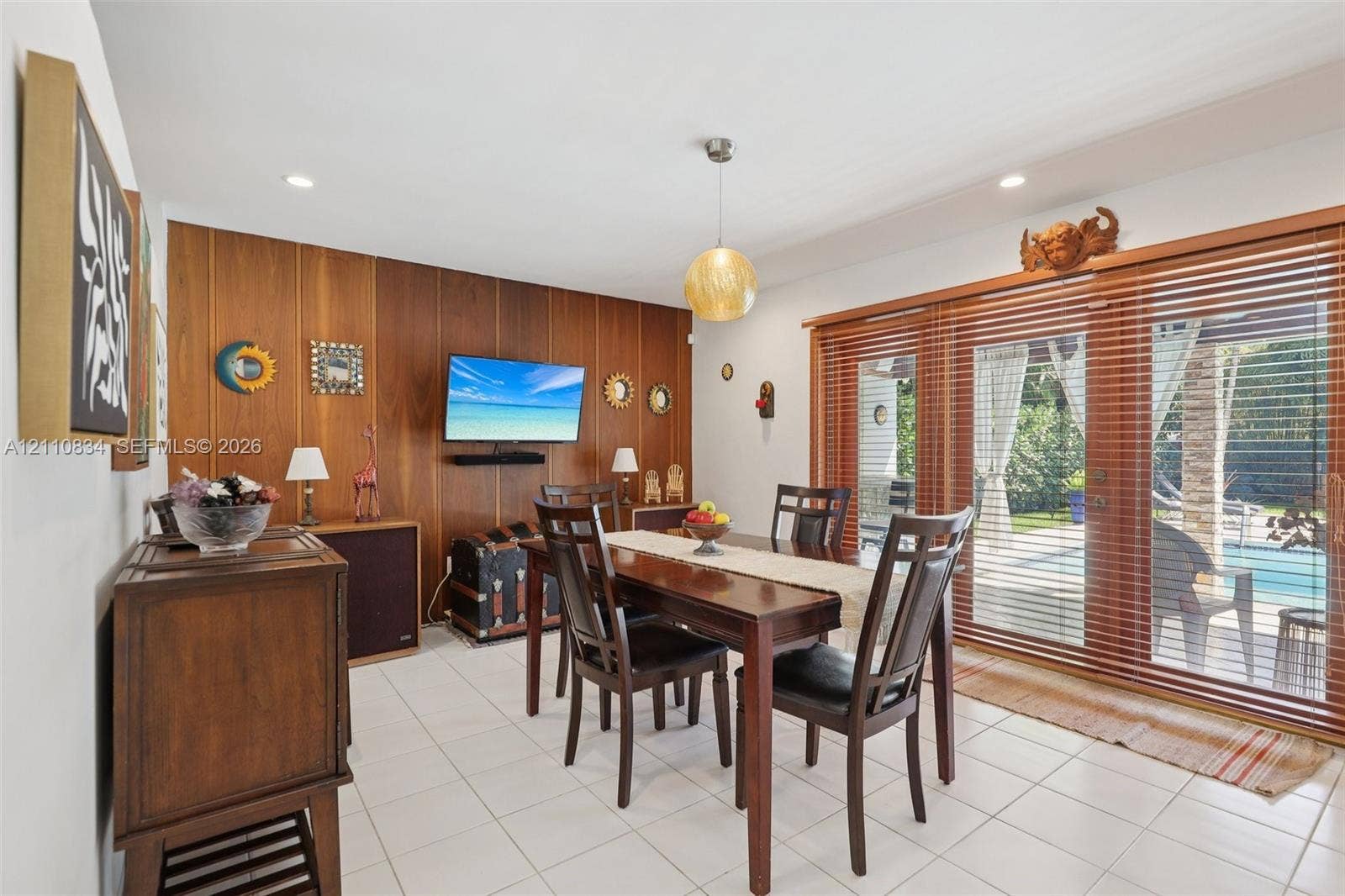 4120 SW 15th Street, Miami, FL 33142 Dining area featuring white tile flooring, wood-paneled accent wall, recessed lighting, spherical pendant light, and sliding glass doors with wood blinds