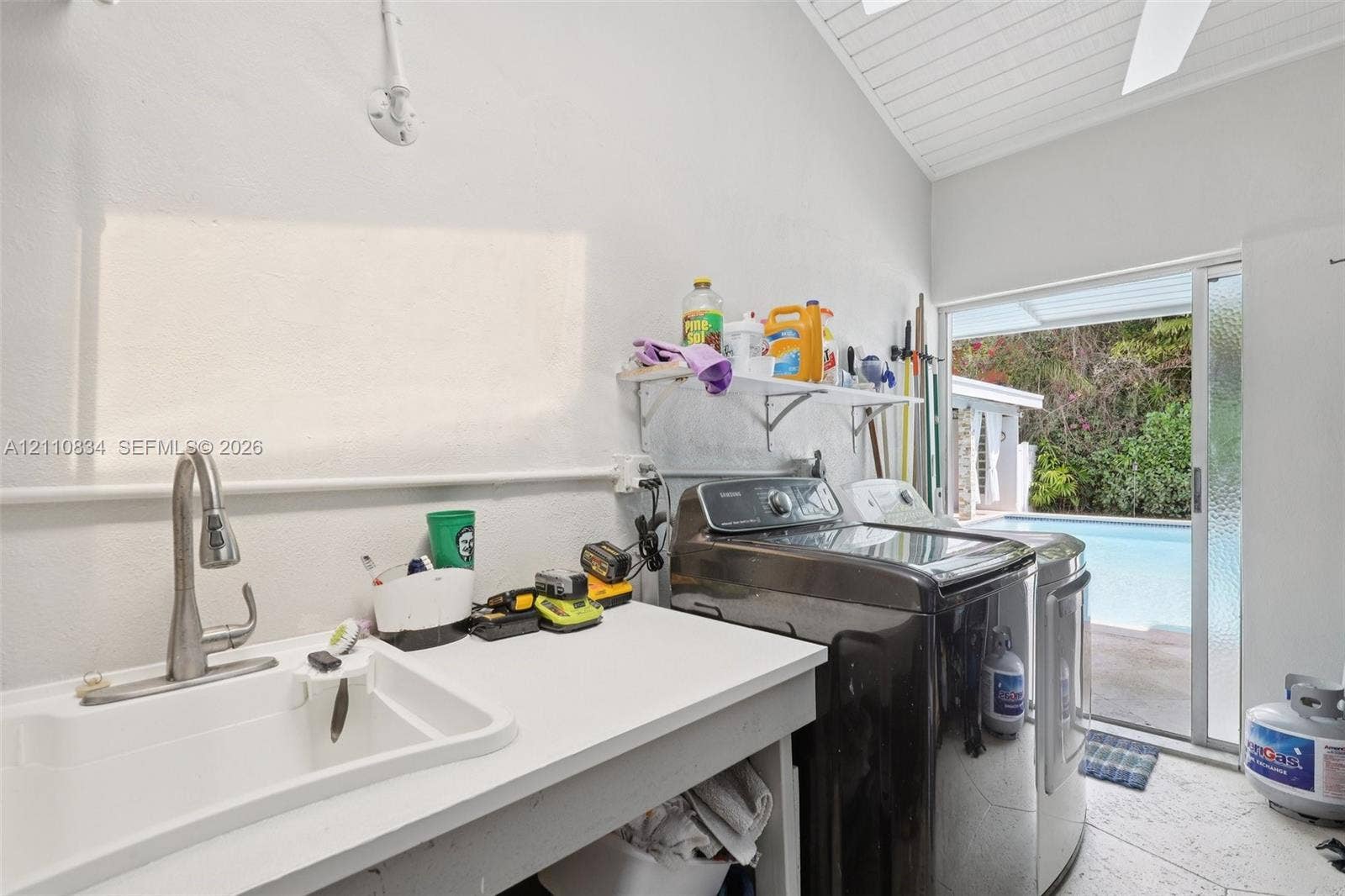 4120 SW 15th Street, Miami, FL 33142 Laundry area featuring a utility sink with a high-arch pull-down faucet, vaulted ceiling with tongue-and-groove finish, tile flooring, and glass sliding door access to the exterior pool area