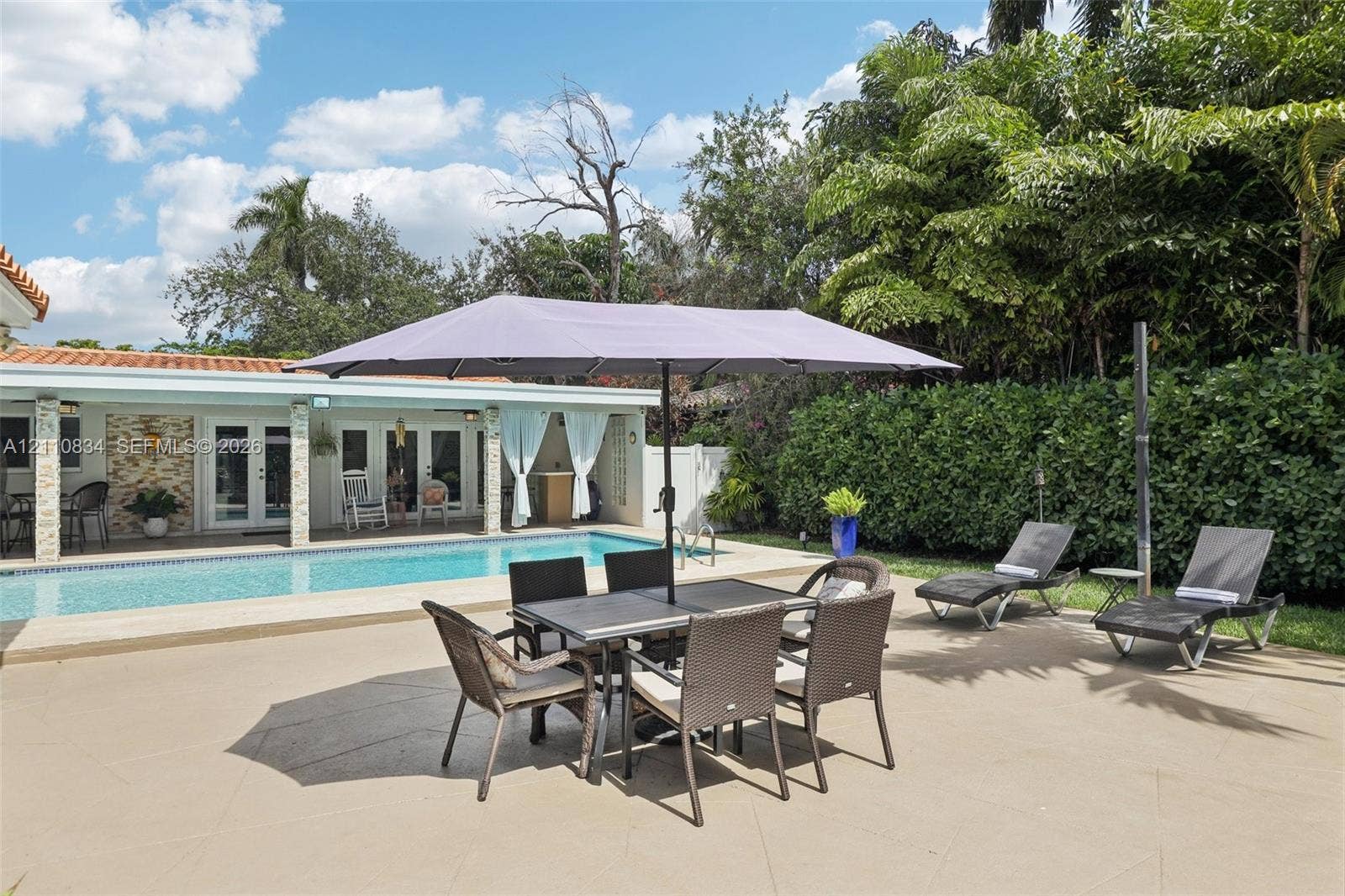 4120 SW 15th Street, Miami, FL 33142 Spacious paved patio featuring an in-ground swimming pool, stone-accented exterior wall, and dense mature perimeter landscaping