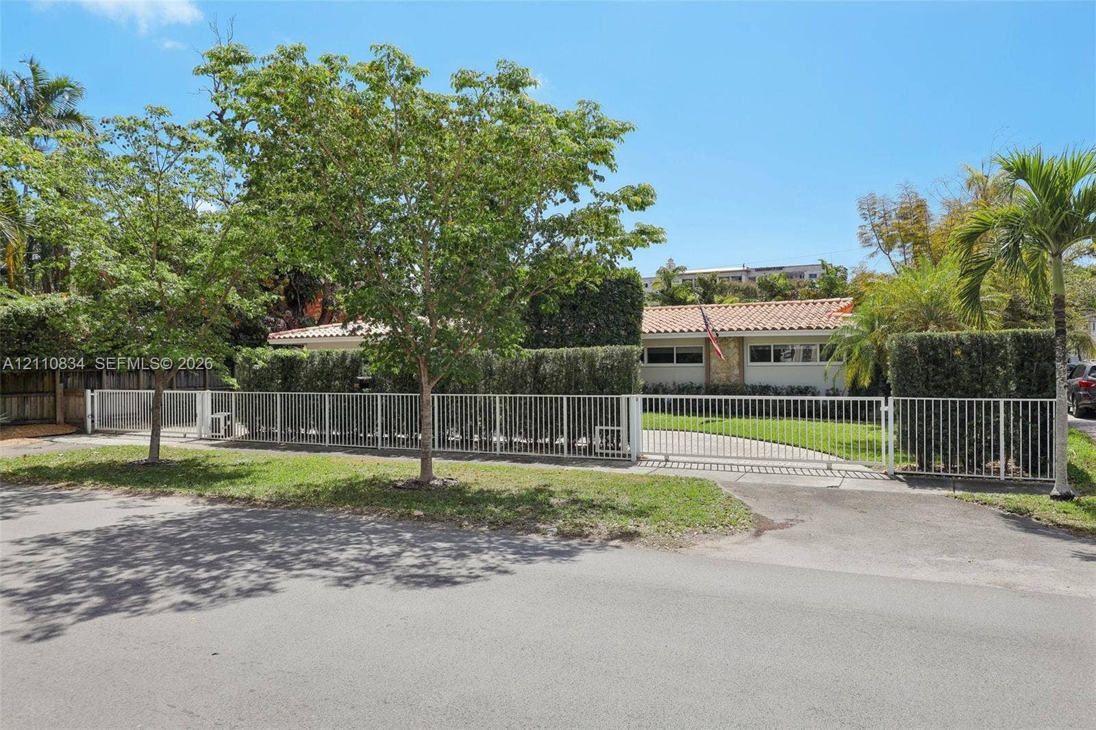 4120 SW 15th Street, Miami, FL 33142 Single-story residence featuring a terracotta-tiled roof, stone-accented facade, gated paved driveway, and mature landscaping