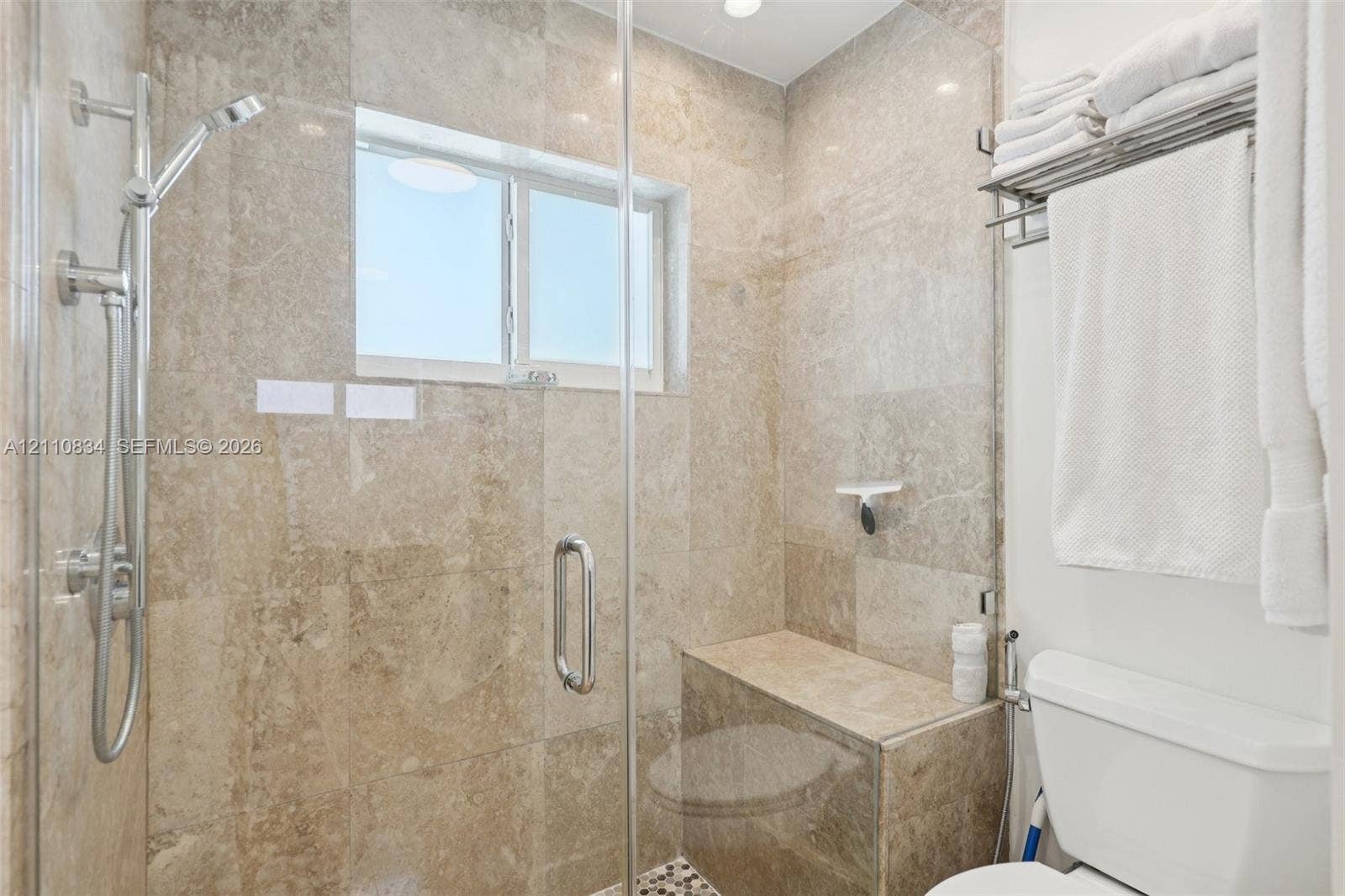 4120 SW 15th Street, Miami, FL 33142 Walk-in shower enclosure featuring floor-to-ceiling stone-tile surround, built-in stone bench, glass door, and wall-mounted adjustable shower head