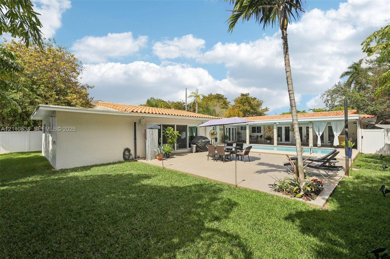 4120 SW 15th Street, Miami, FL 33142 Rear exterior featuring a concrete patio, rectangular swimming pool, clay tile roof, and enclosed yard with perimeter fencing