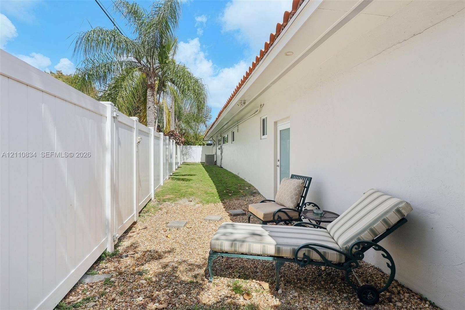 4120 SW 15th Street, Miami, FL 33142 Side exterior featuring stucco siding, clay tile roof eaves, white vinyl privacy fencing, and a gravel ground cover