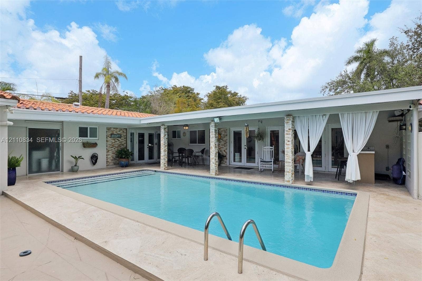 4120 SW 15th Street, Miami, FL 33142 In-ground swimming pool with stone-tiled decking and covered patio area featuring stone-clad support columns and light-toned exterior finish