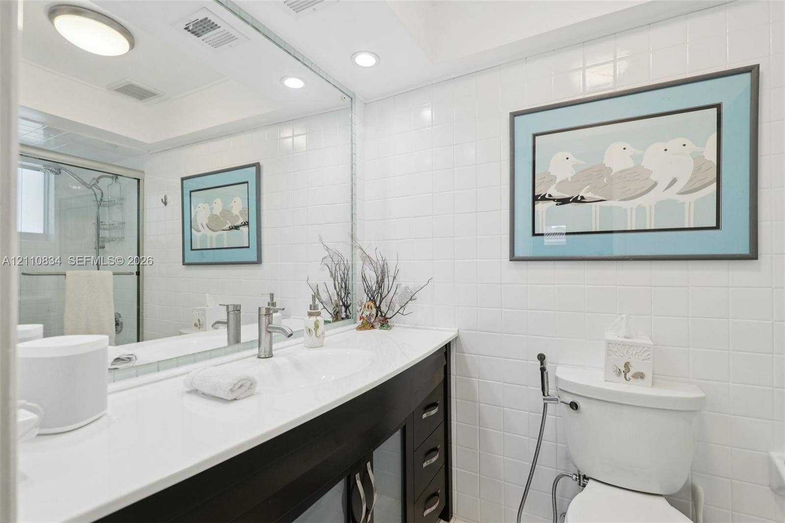 4120 SW 15th Street, Miami, FL 33142 Bathroom vanity featuring a solid surface countertop, integrated sink, dark-toned cabinetry, full-width mirror, and shower enclosure with a glass door