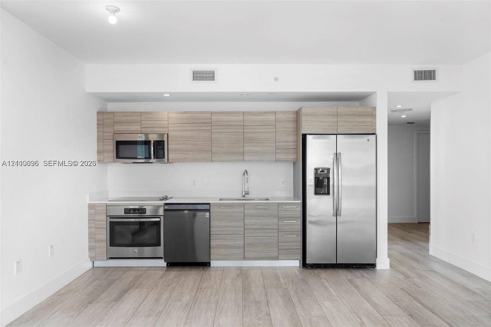 Kitchen featuring wood-finish cabinetry, stainless steel appliances, a flat-top range, and light-toned wood-finish flooring