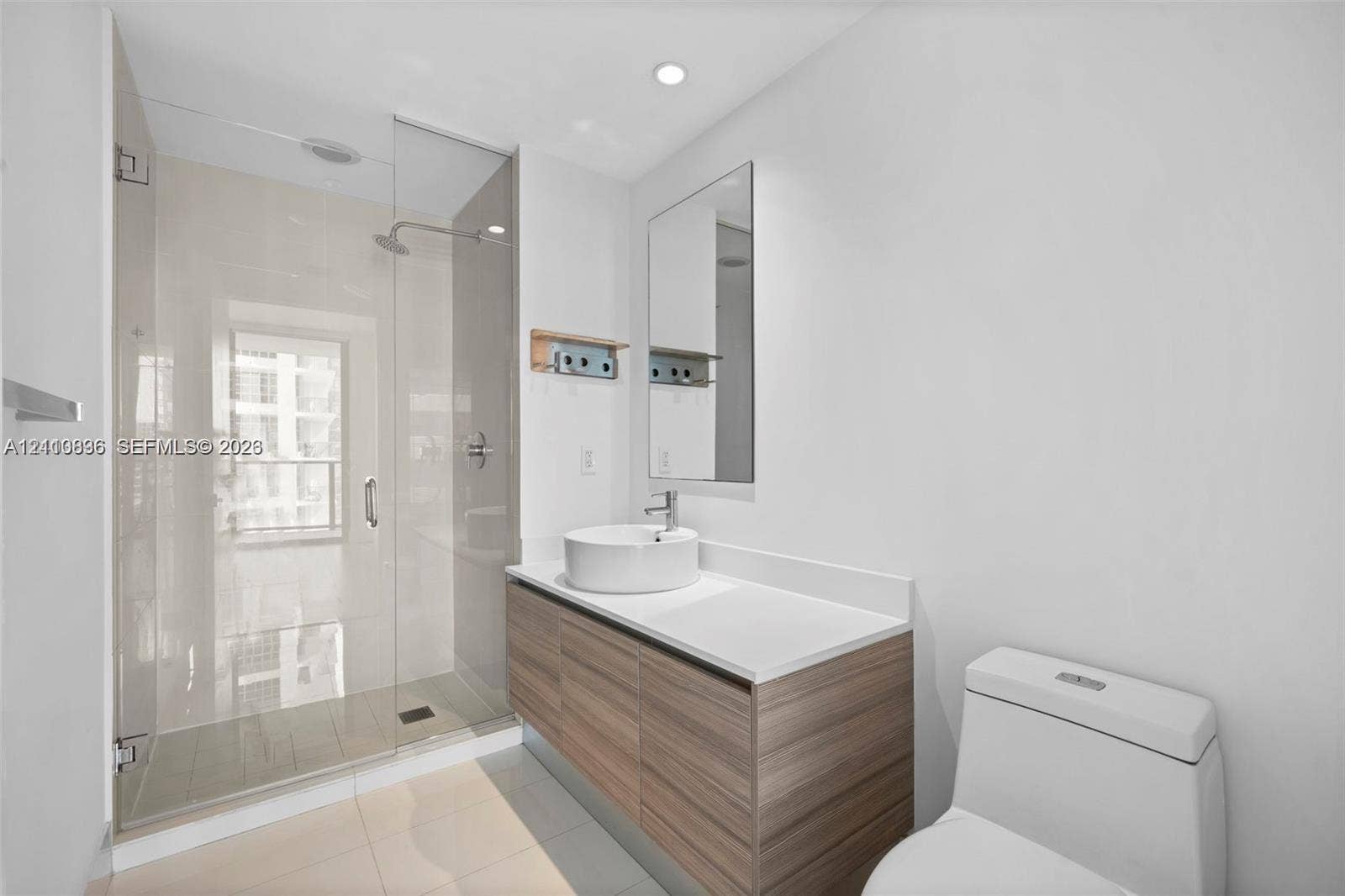Bathroom featuring a wood-finish floating vanity, circular vessel sink, white solid-surface countertop, and a walk-in glass-enclosed shower with polished chrome fixtures