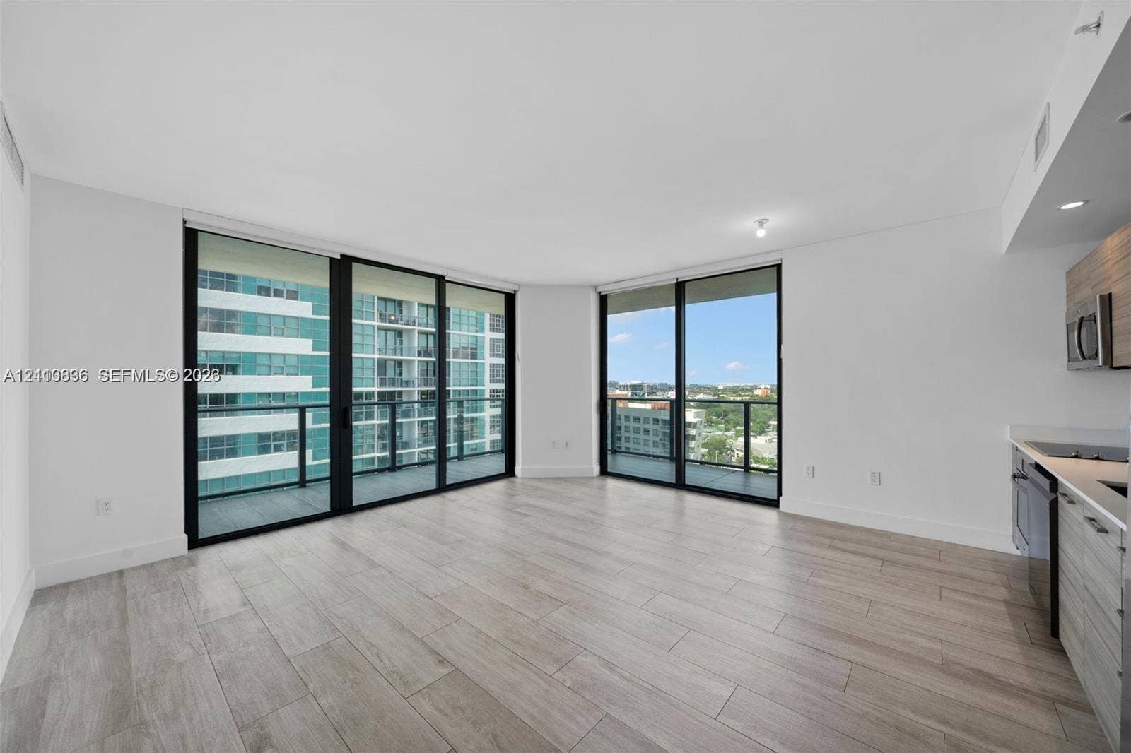 Floor-to-ceiling sliding glass doors, neutral wood-finish flooring, recessed lighting, and kitchen cabinetry featuring a contemporary wood-grain finish