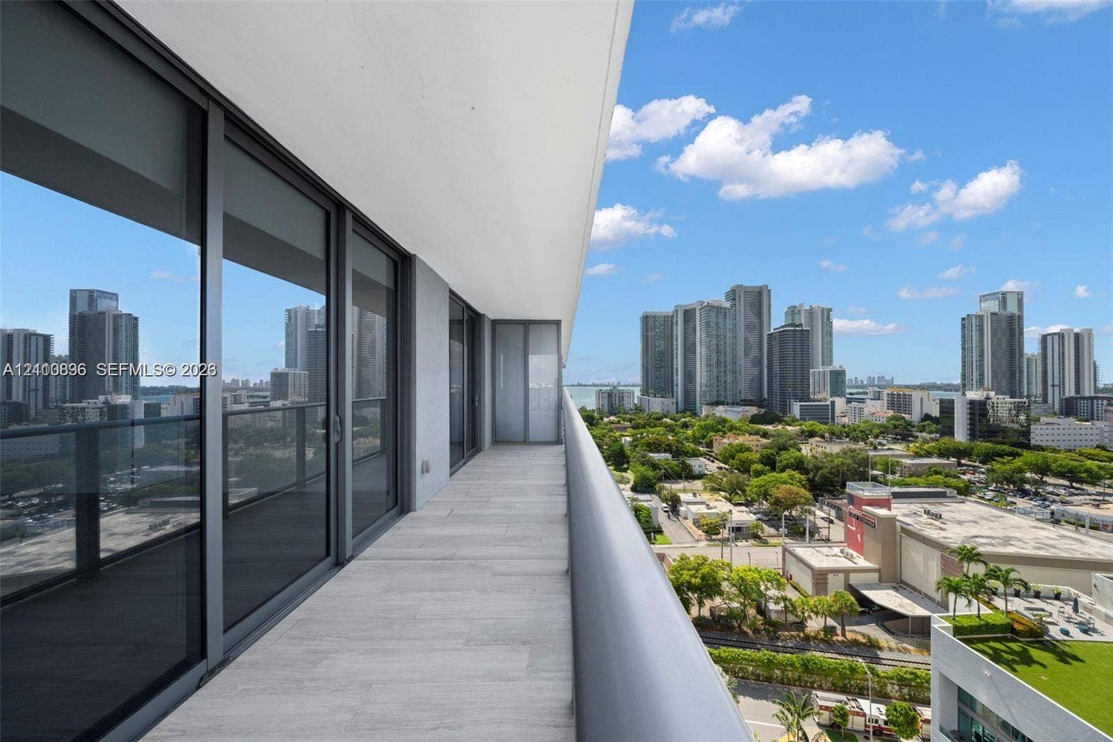 Expansive covered terrace featuring large-format tile flooring, floor-to-ceiling glass sliding doors, and a sleek metal railing