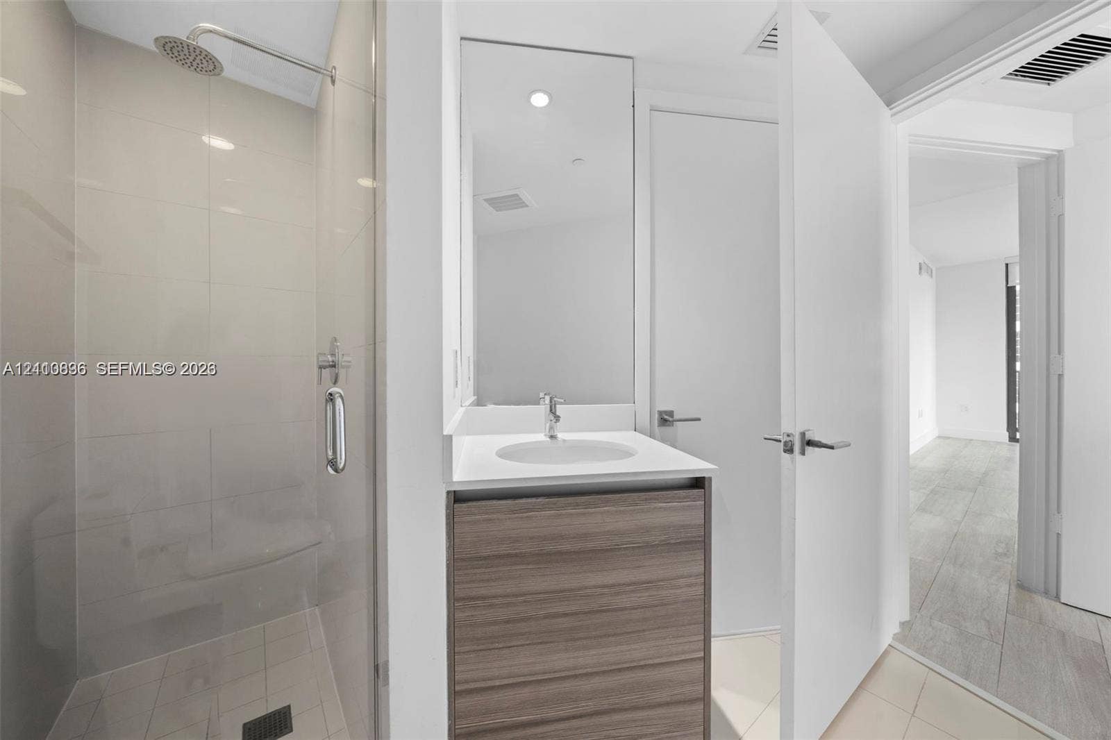 Glass-enclosed shower with rainfall showerhead, wood-finish vanity with countertop basin, and large-format tile flooring