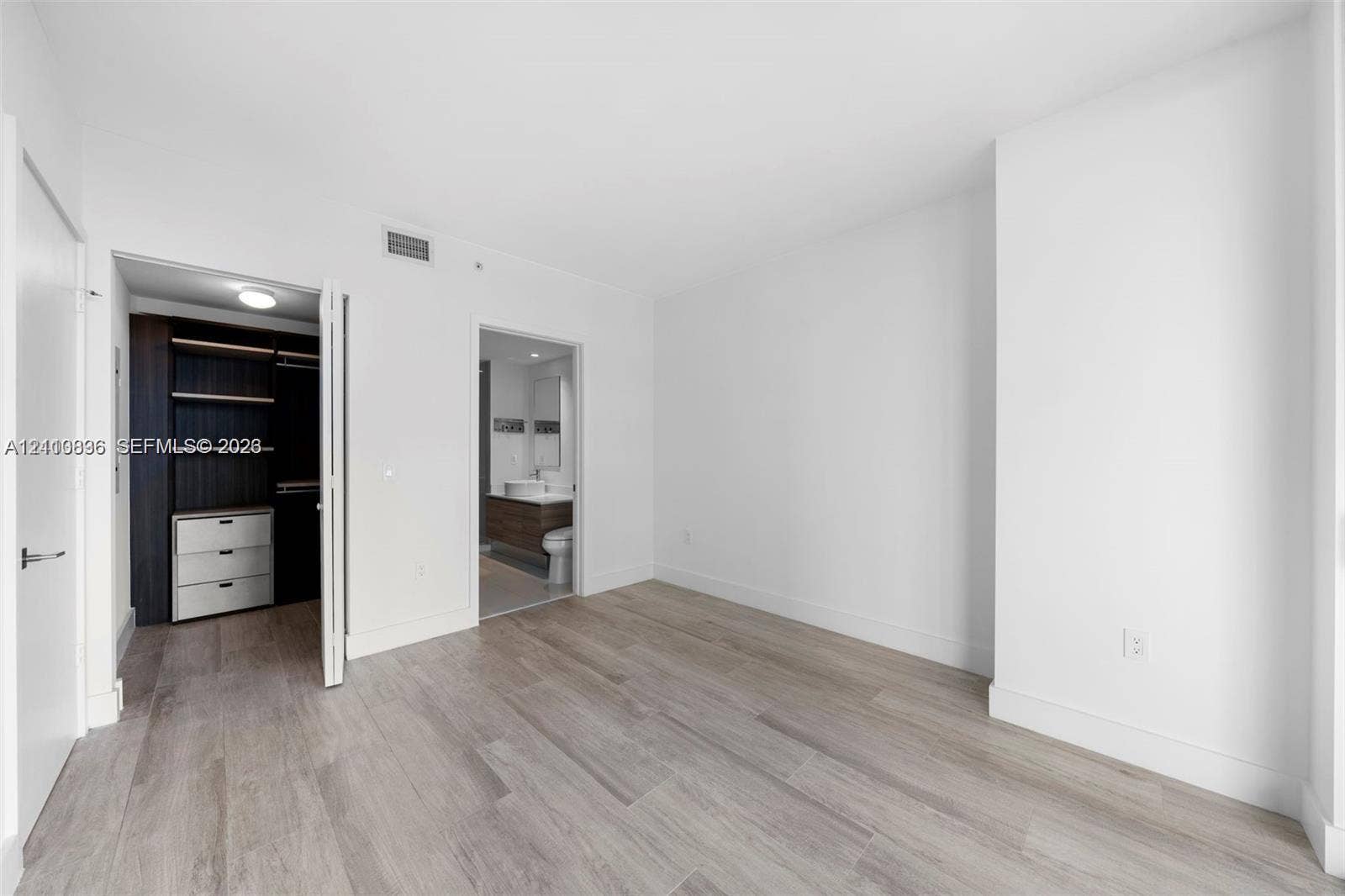 Room featuring wood-finish flooring, built-in closet cabinetry, and a vanity with a vessel sink