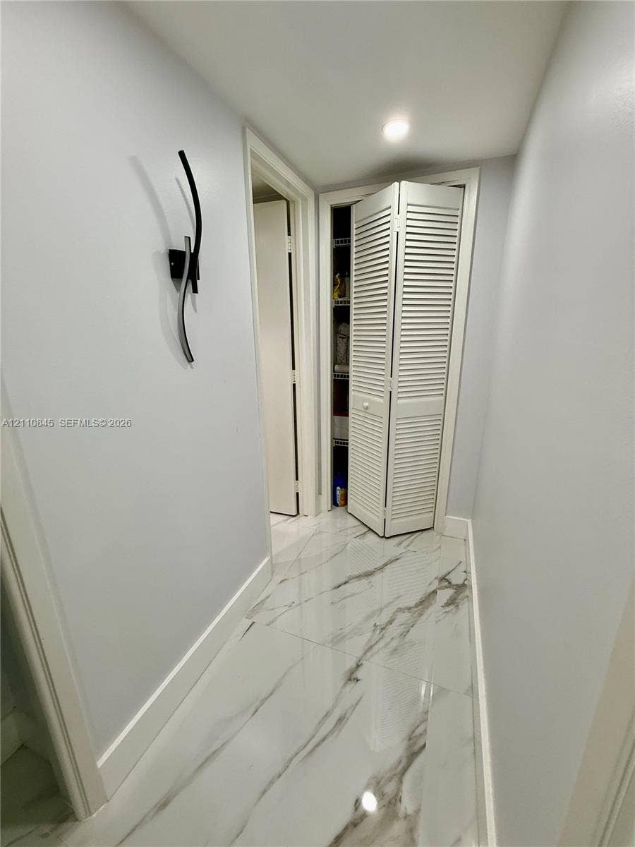 565 Oaks Lane, #410, Pompano Beach, FL 33069 Large-format tile flooring with a neutral-toned veined pattern, louvered bi-fold closet doors, and a contemporary wall-mounted light fixture