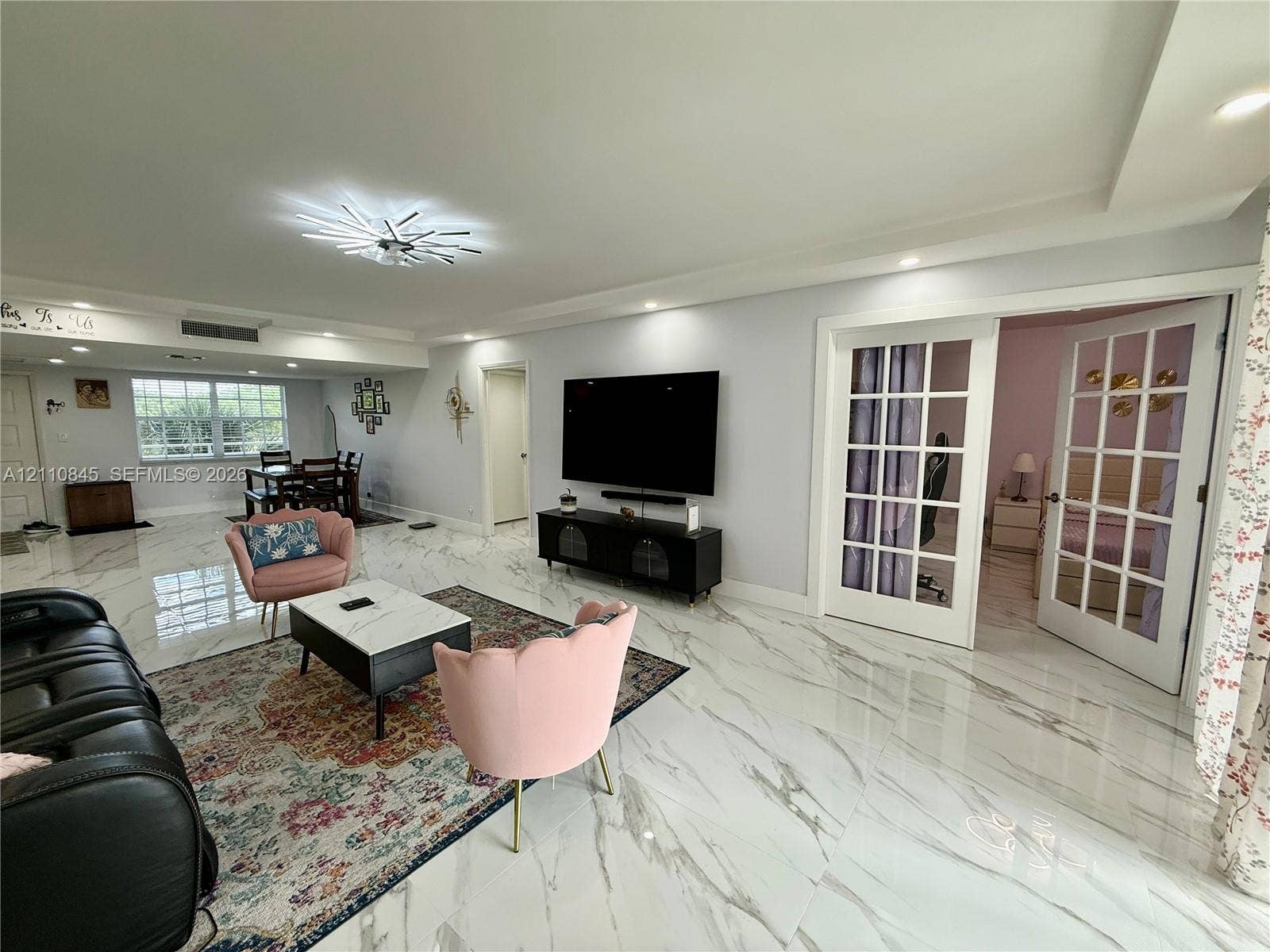 565 Oaks Lane, #410, Pompano Beach, FL 33069 Open-concept interior featuring polished stone-finish flooring, recessed lighting, a modern starburst chandelier, and French doors with glass panes