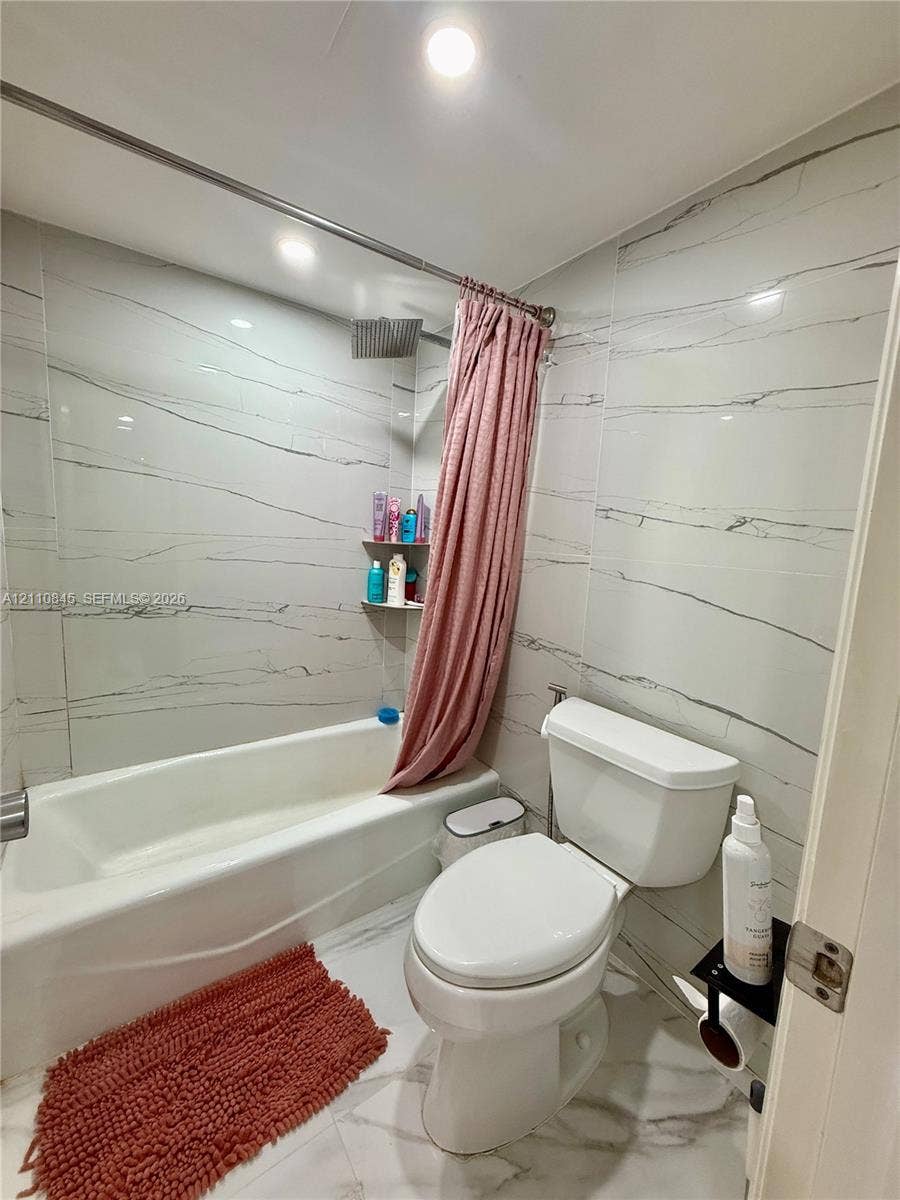 565 Oaks Lane, #410, Pompano Beach, FL 33069 Full-height wall tiling featuring veined detailing, white acrylic bathtub, integrated shower head, recessed ceiling lighting, and large-format tile flooring