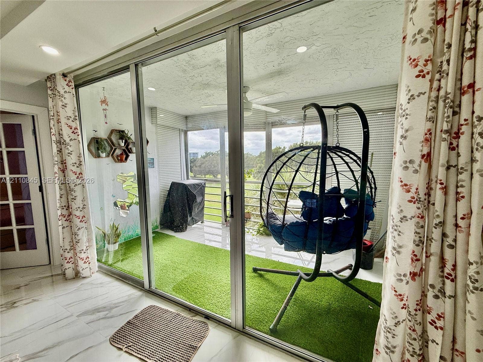 565 Oaks Lane, #410, Pompano Beach, FL 33069 Enclosed balcony featuring floor-to-ceiling glass sliding doors, synthetic turf flooring, ceiling fan, and metal railings