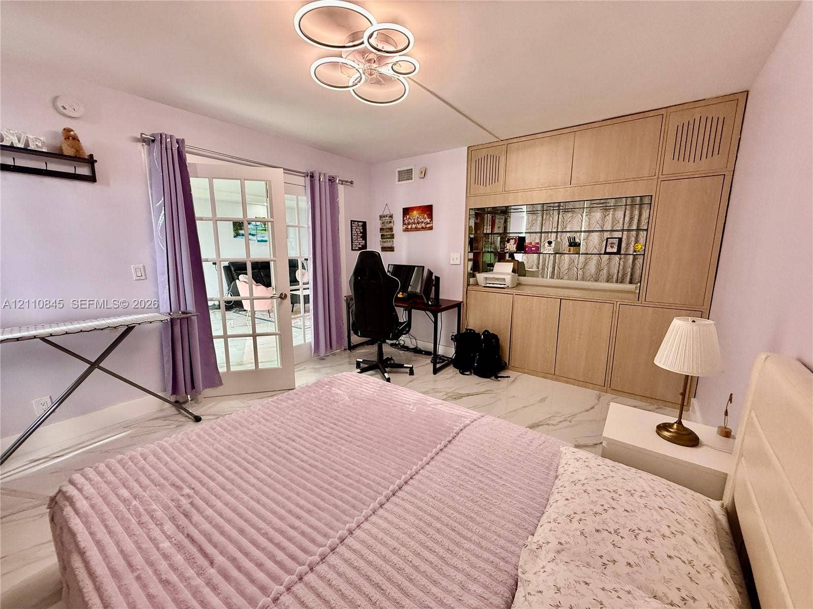 565 Oaks Lane, #410, Pompano Beach, FL 33069 Large-format tile flooring, integrated floor-to-ceiling wooden cabinetry with a built-in mirrored display section, multi-tiered circular LED light fixture, and double French doors with glass panes